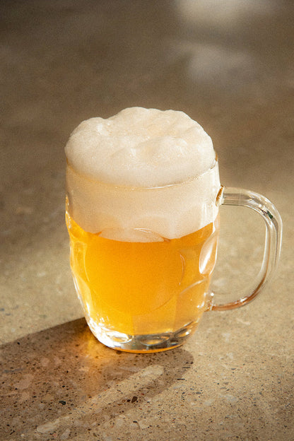 Glass mug of beer with a head of foam on a textured surface
