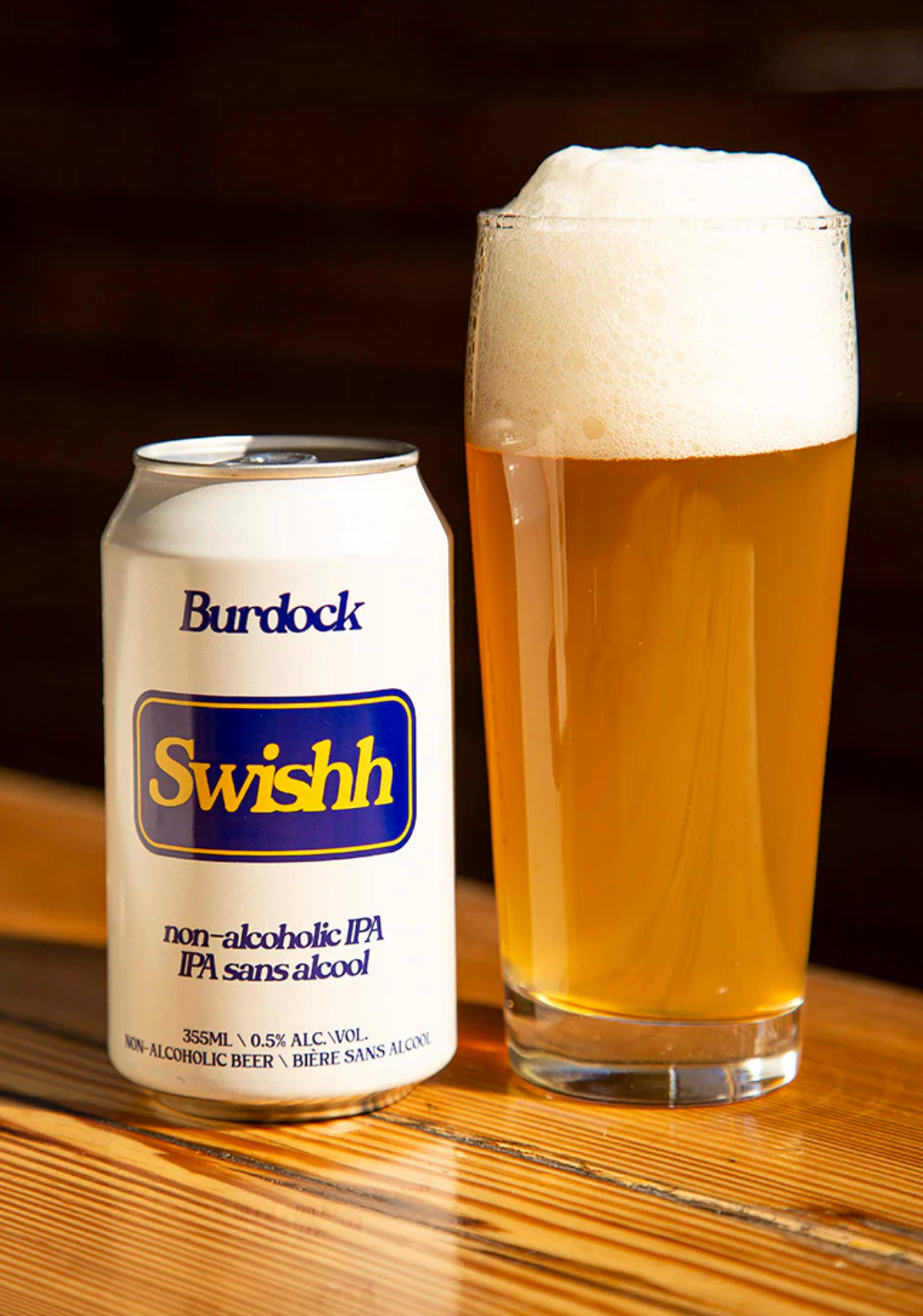 Burdock Swishh non-alcoholic IPA can and glass of beer on a wooden surface