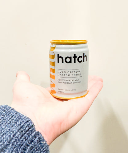 Hand holding a can of 'hatch' cold oatado against a plain background