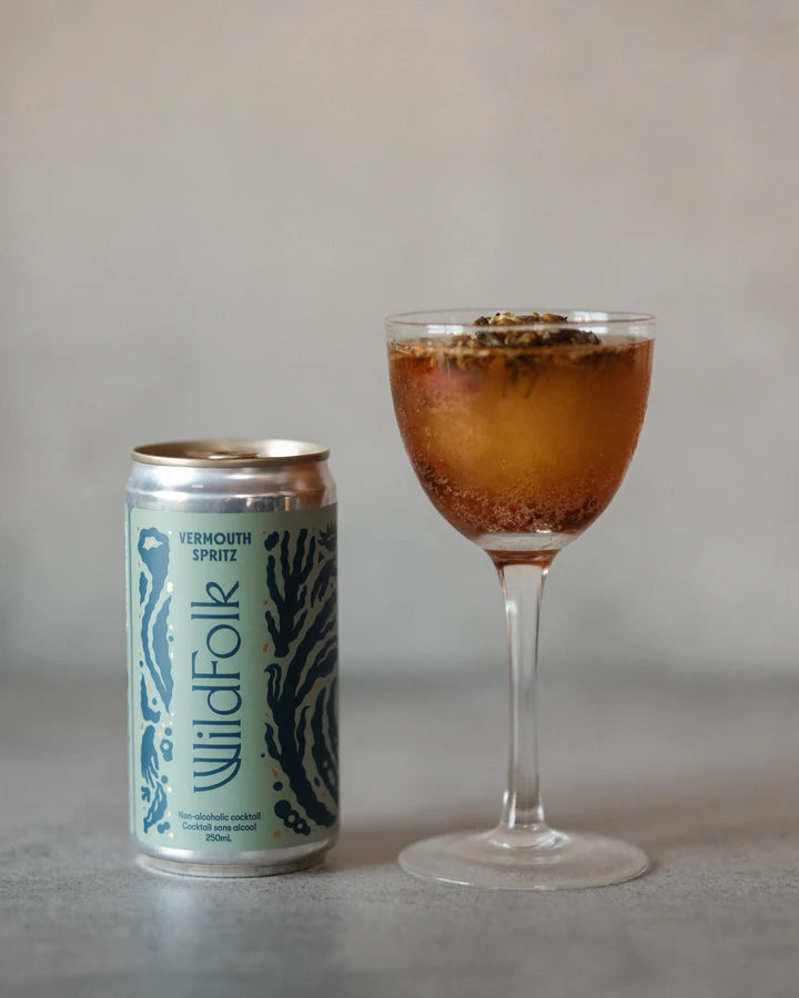 Cocktail in a glass with a can labeled 'Wildfolk' on a neutral background
