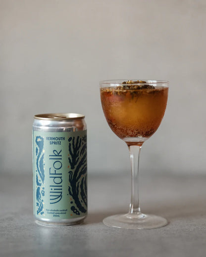 Cocktail in a glass with a can labeled 'Wildfolk' on a neutral background